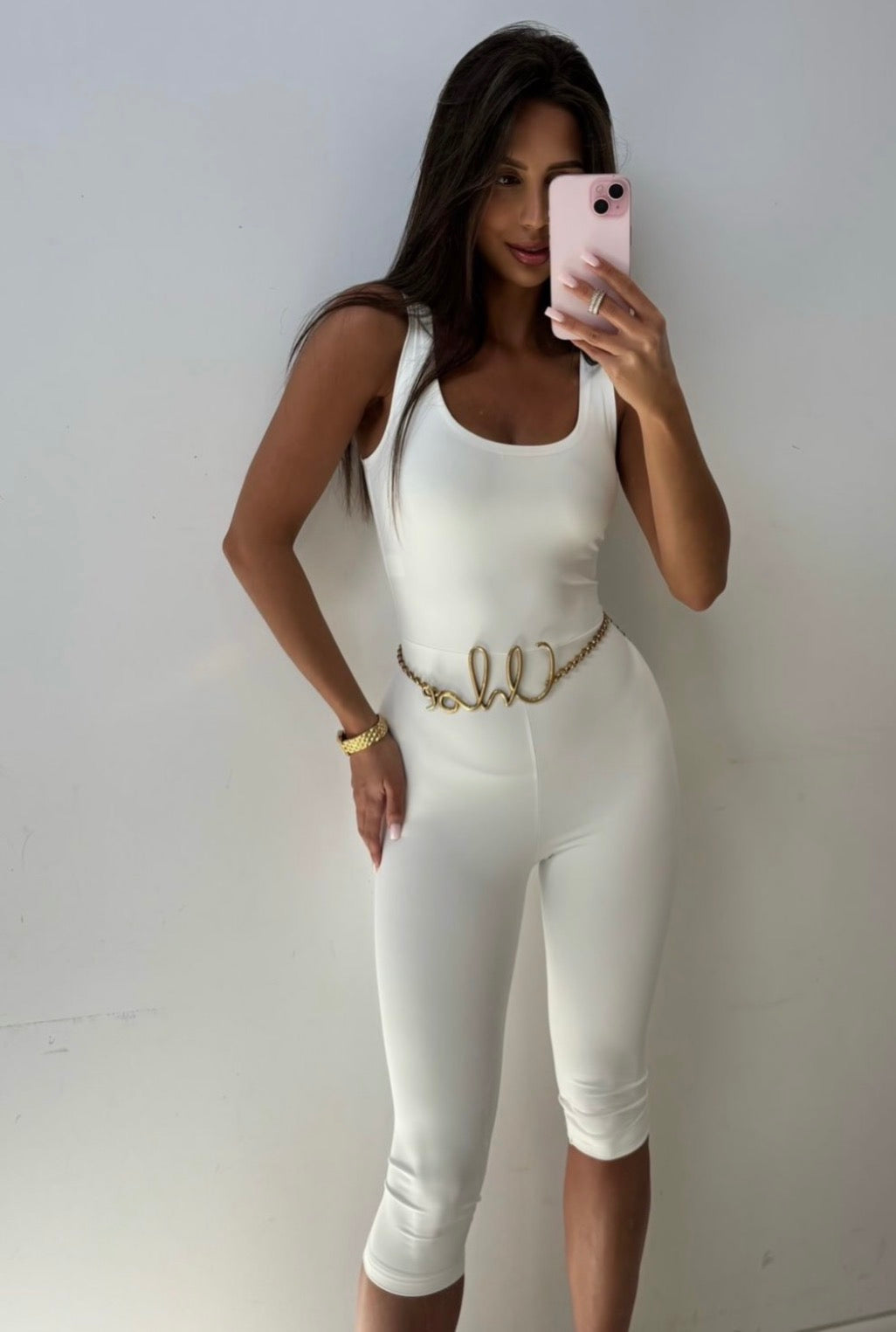 Liv white capri jumpsuit styled with a gold waist belt, front view